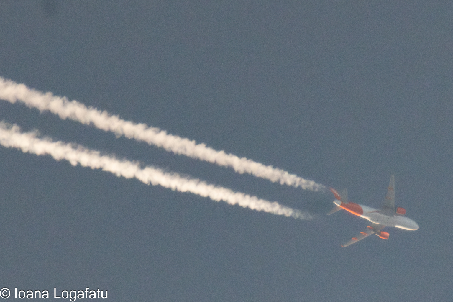 Bright orange aircraft glides through a clear sky